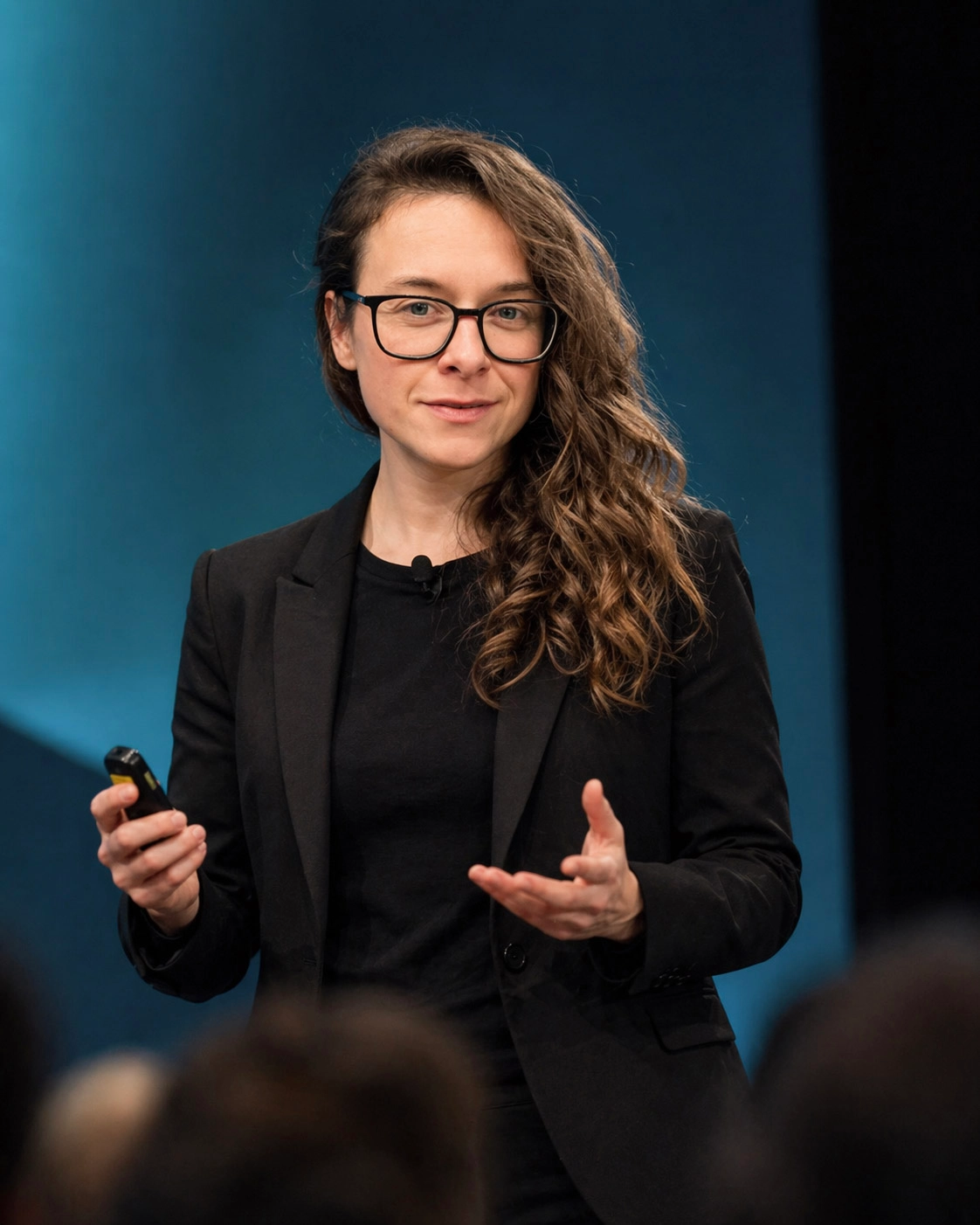 Laurence Paquette speaking on stage at a keynote, gesturing while holding a presentation clicker.