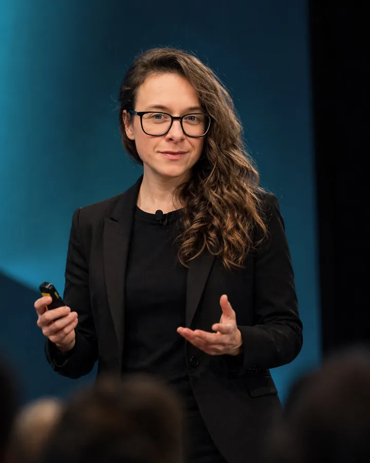 Laurence Paquette speaking on stage, holding a presentation clicker.